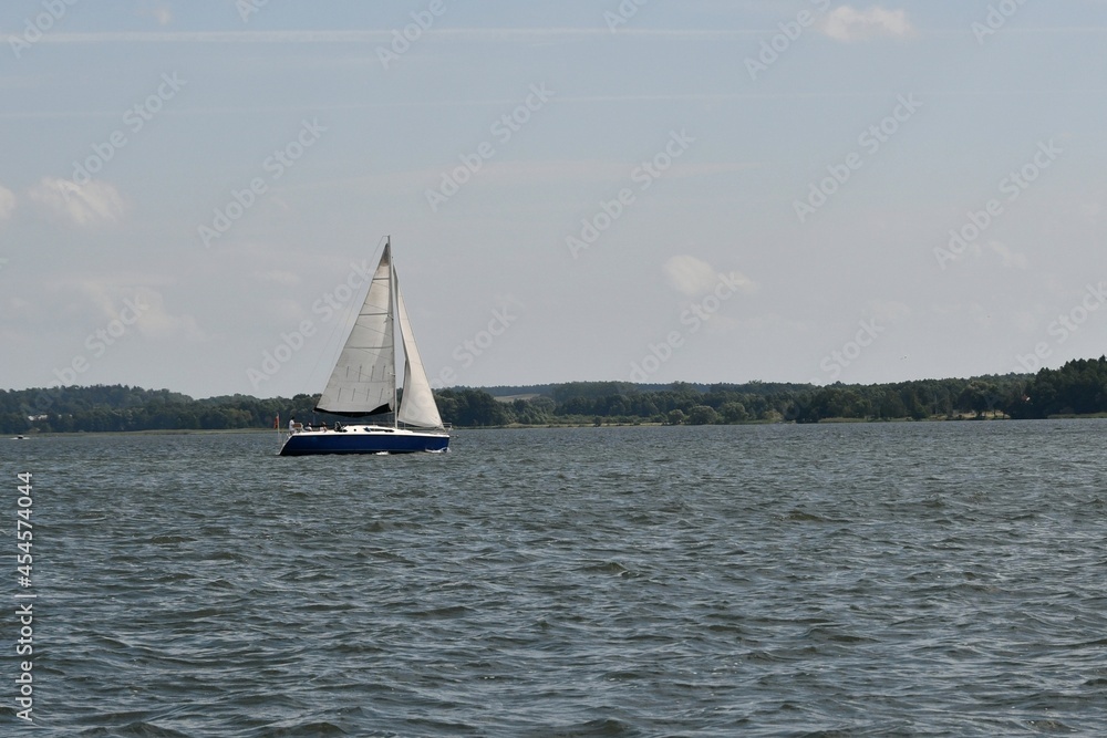 Sylwetka samotnie żeglujacego jachtu kabinowego. Mazury, krajobraz.