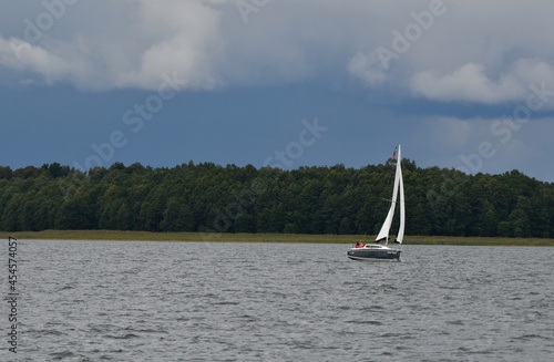 Sylwetka samotnie żeglujacego jachtu kabinowego po jeziorze. Mazury, krajobraz.