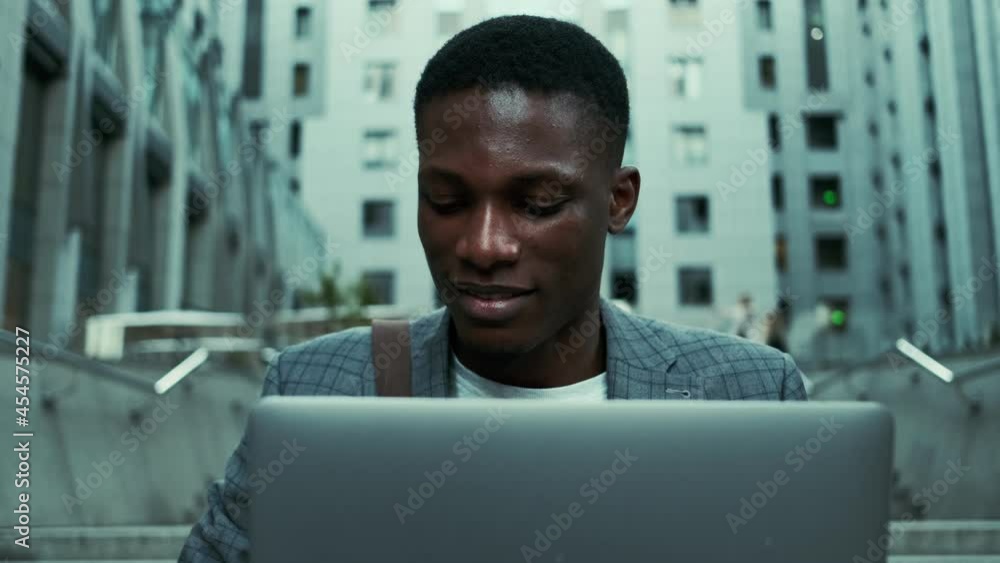 A concentrated african american businessman working with his laptop outside on the street A concentrated african american businessman working with his laptop outside on the street