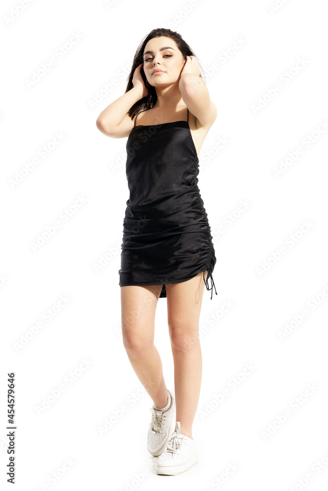 Confident cool cocky gen Z young beauty woman in black satin dress posing with hands in hair. Full body portrait isolated on white background Confident cool cocky gen Z young beauty woman in black satin dress posing with hands in hair. Full body portrait isolated on white background