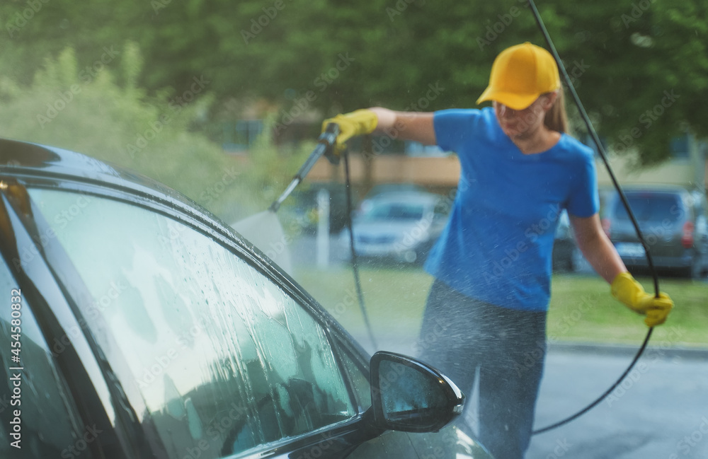 Woman in uniform cleaning car using high pressure water. Car wash service. Woman in uniform cleaning car using high pressure water. Car wash service.
