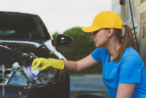 Woman in uniform cleaning car with sponge. Car wash service.
