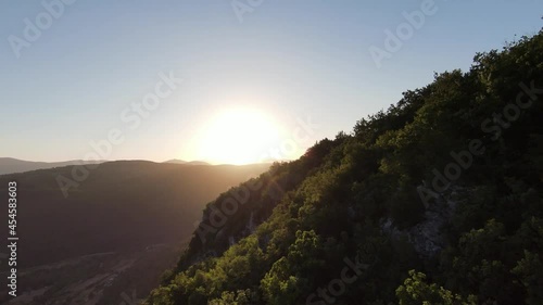 Aerial cinematic shot high speed sport fpv drone flying over natural mountain cliff canyon country road surrounded Amazing nature rocky terrain with green vegetation and forest on sunset.  photo