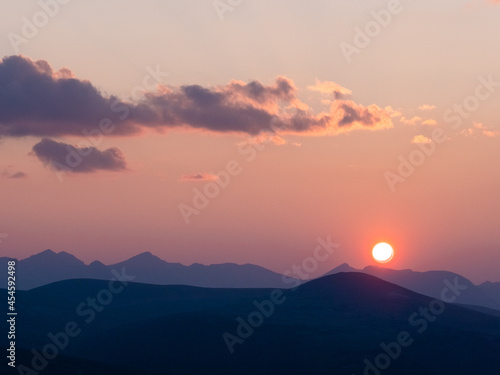 Sun setting over the peaks of the rocky mountains with pastel colored sky and pretty clouds.