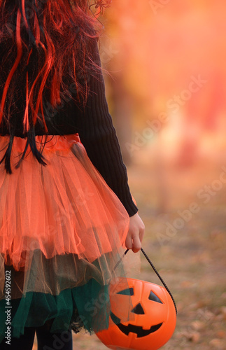 Little girl in witch costume with a balloon and a pumpkin bucket playing in autumn park. Child having fun at Halloween trick or treat. Kids trick or treating. photo