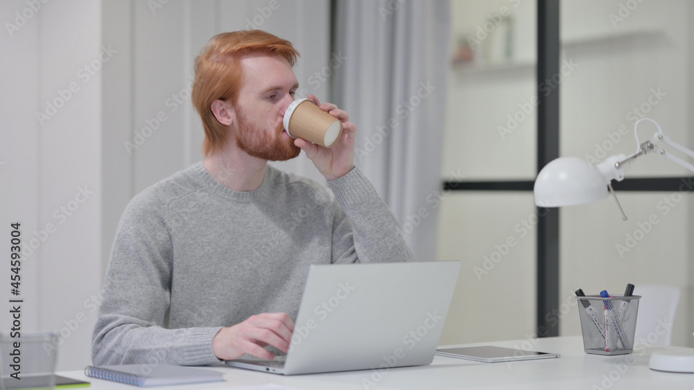 Beard Redhead Man Drinking Coffee While Typing on Laptop Beard Redhead Man Drinking Coffee While Typing on Laptop
