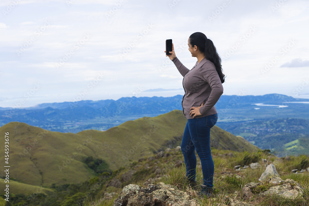 woman standing on the mountain taking picture with mobile