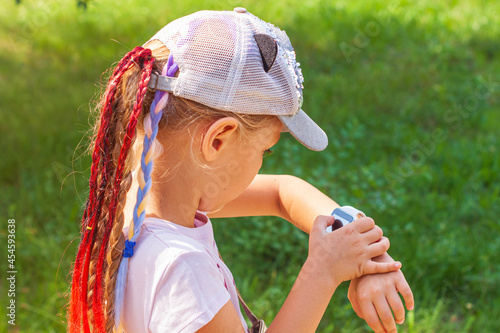 Child schooler using smartwatch outdoor park. Kid talking on vdeo call with parents on smartwatches. Schoolgirl searching on the internet using watches touchscreen display.Smart wristwatch GPS tracker