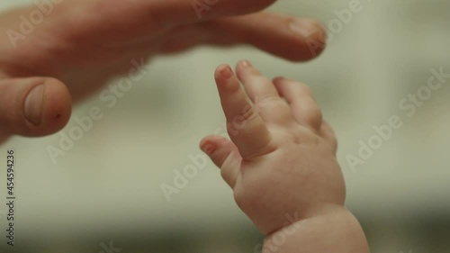 Close-up shot of baby's little cute hand reaching for father's loving finger . Baby holding parent's finger . Parent holding newborns hand in Slow Motion . Hand in hand. Father and his newborn baby . 