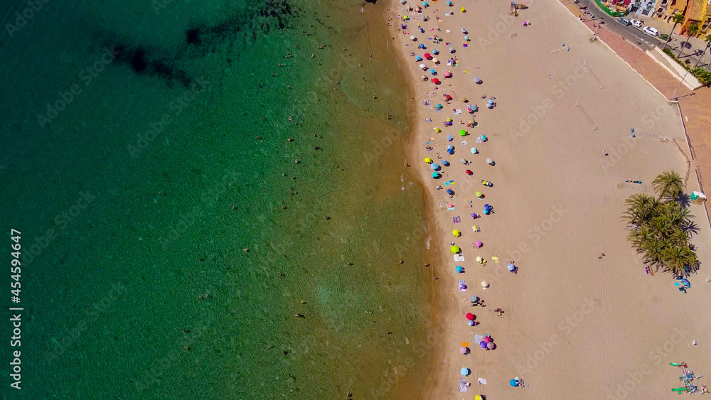 Tomas cenitales y aéreas de la ciudad y la playa de Villajoyosa en Alicante con gente tomando el sol con sus sombrillas y bañándose en el mar