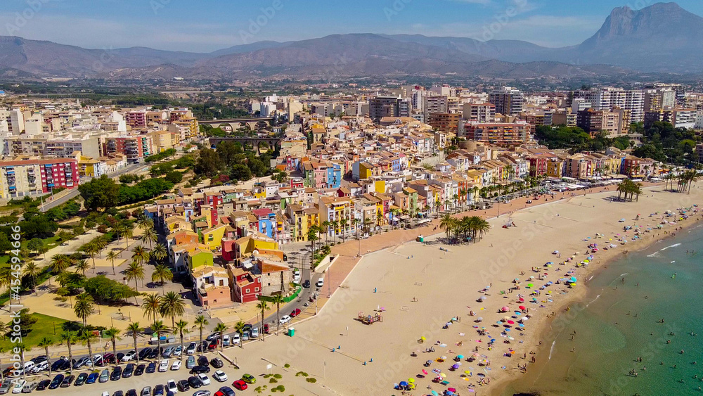 Obraz premium Tomas cenitales y aéreas de la ciudad y la playa de Villajoyosa en Alicante con gente tomando el sol con sus sombrillas y bañandose en el mar