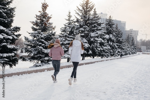 Two young athletic girls running in the park on a sunny winter day. A healthy way of life.