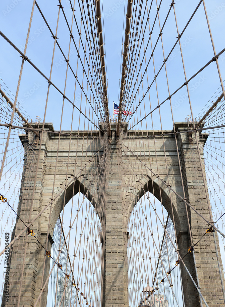 Obraz premium The American flag on the Brooklyn Bridge flies a bright day in the summer