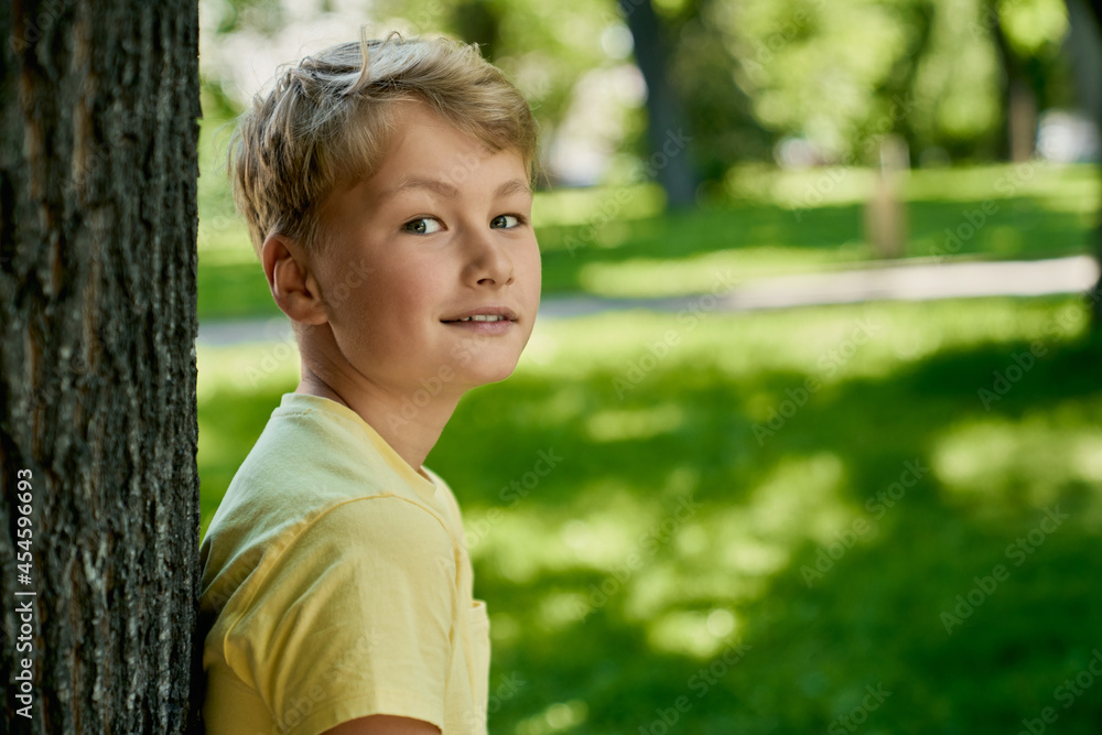 Cute caucasian boy in casual wear posing near tree at green park. Happy child spending free time on fresh air. Summer warm days. Cute caucasian boy in casual wear posing near tree at green park. Happy child spending free time on fresh air. Summer warm days.