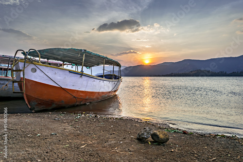 Beautiful sunset behind a parked red and white boat at shore in Bamnoli, Maharashtra,India.