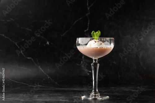 Glass of ice cold Baileys cocktail served in a coupe glass, decorated with mint leaf placed on a black background photo