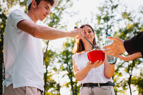 A couple of volunteer helping one homeless man giving to him a bowl of soup and a plastic bottle of water, volunteer mission concept.