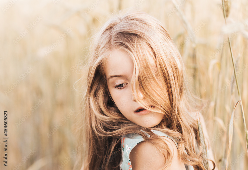 Beautiful little girl blonde with long hair walking through a wheat field