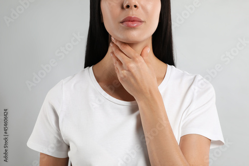 Young woman doing thyroid self examination on light background, closeup photo