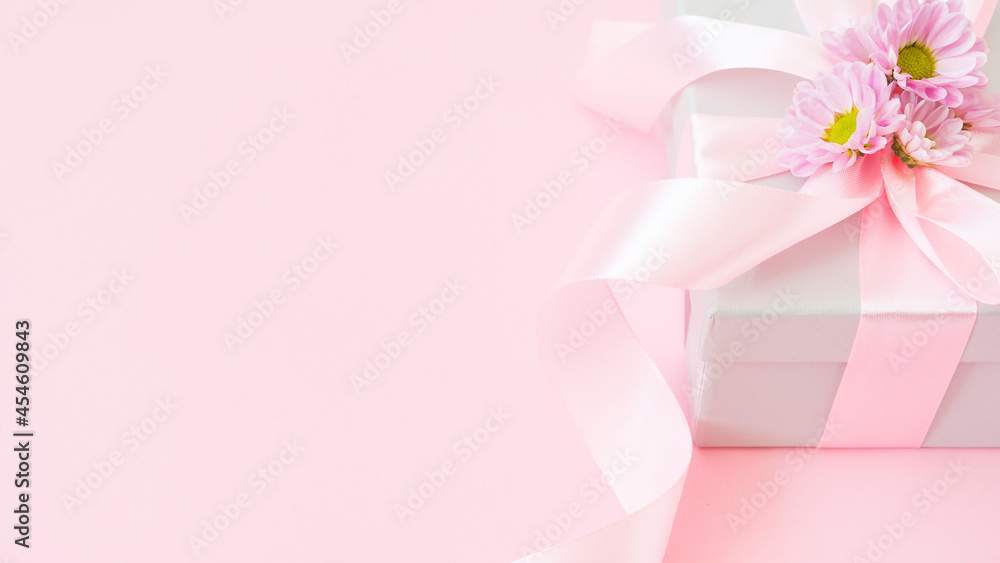 Gift box tied with a pink ribbon and decorated with flowers on a pink background