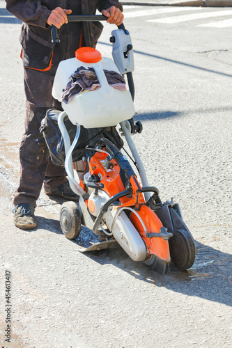 A road worker cuts old asphalt on the road with a portable petrol cutter.