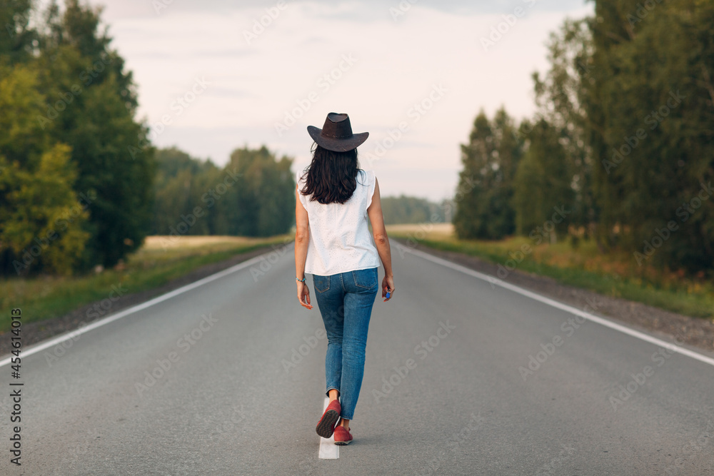 Woman with hat walking on the road dressed jeans.