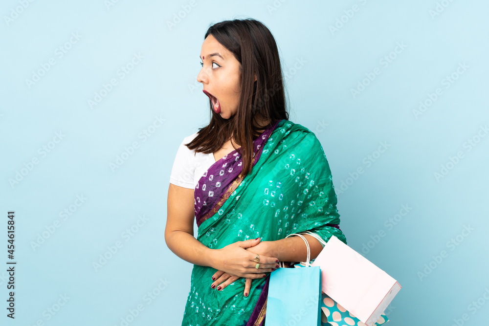 Obraz premium Young Indian woman with shopping bags doing surprise gesture while looking to the side
