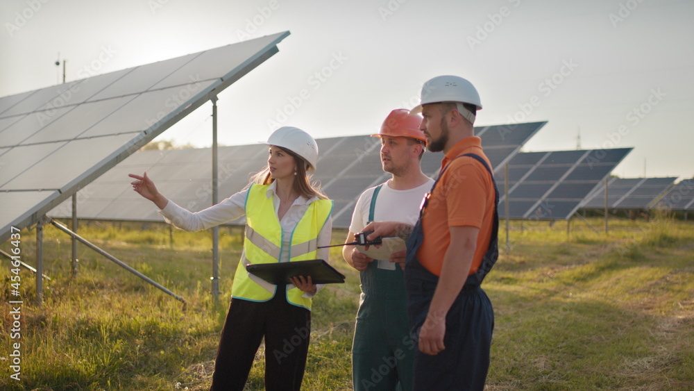 Three solar energy specialists at a solar power facility. Professional engineers discuss innovative project. Team of industrial technicians in solar park. Construction of solar power plant.