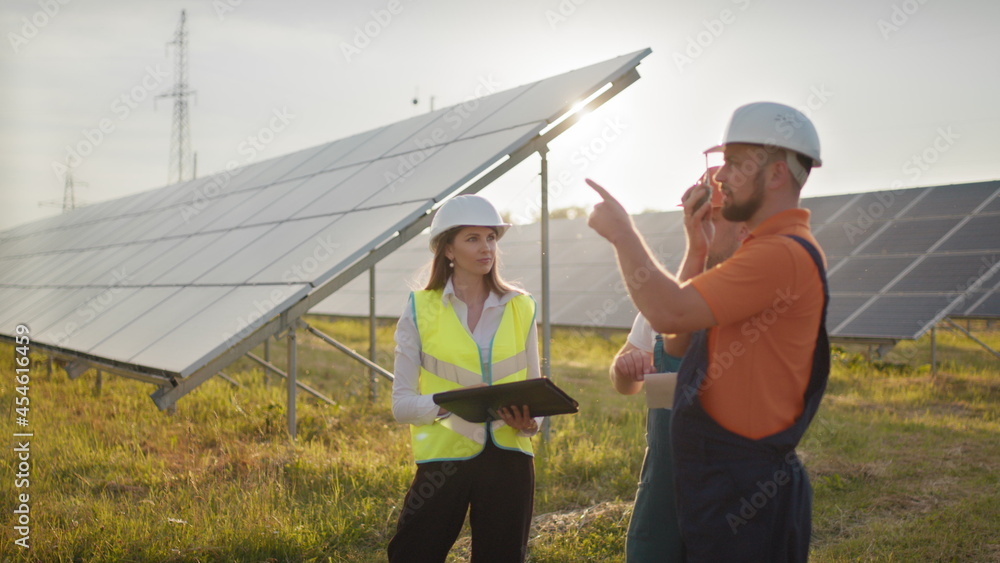 Three solar energy specialists at a solar power facility. Professional engineers discuss innovative project. Team of industrial technicians in solar park. Construction of solar power plant.