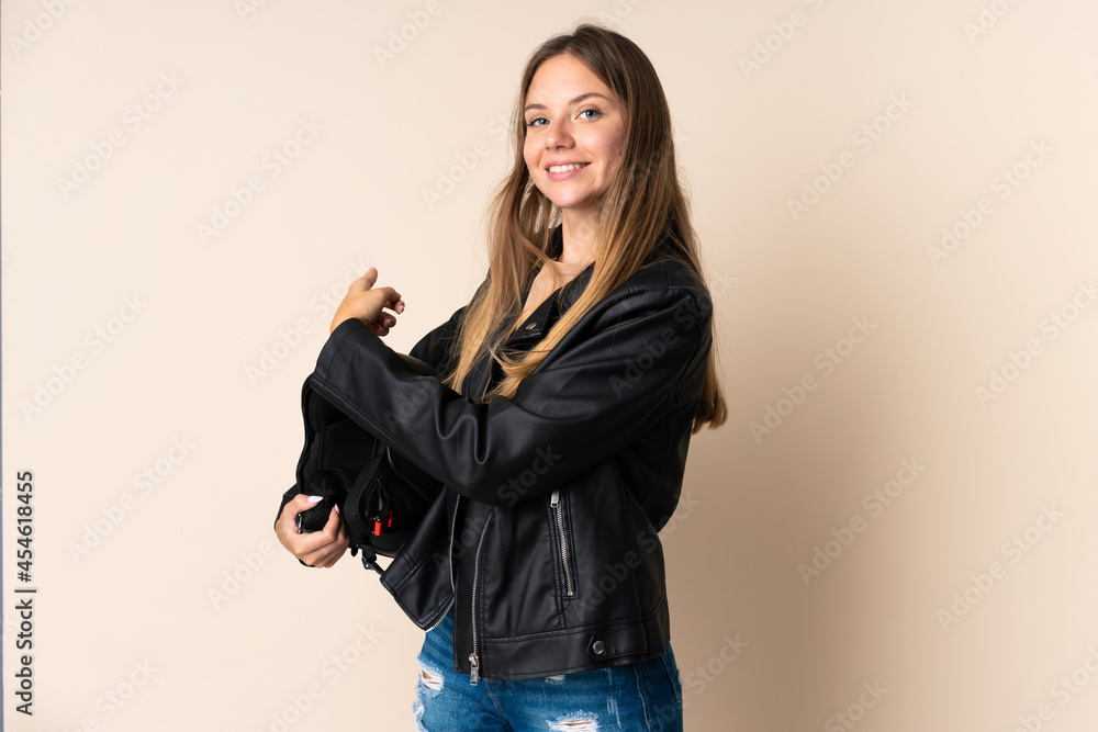 Young Lithuanian woman holding a motorcycle helmet isolated on beige background pointing back Young Lithuanian woman holding a motorcycle helmet isolated on beige background pointing back