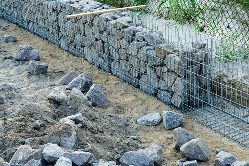 unfinished gabion fence wall construction from steel mesh with stones photo