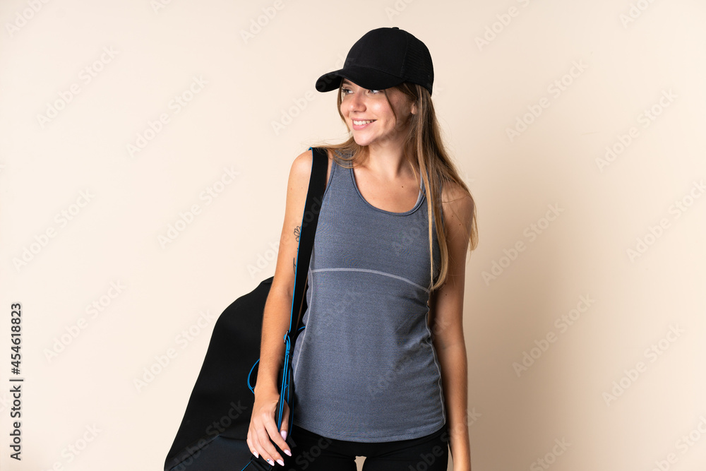 Young sport Lithuanian woman holding a sport bag isolated on beige background looking to the side and smiling Young sport Lithuanian woman holding a sport bag isolated on beige background looking to the side and smiling