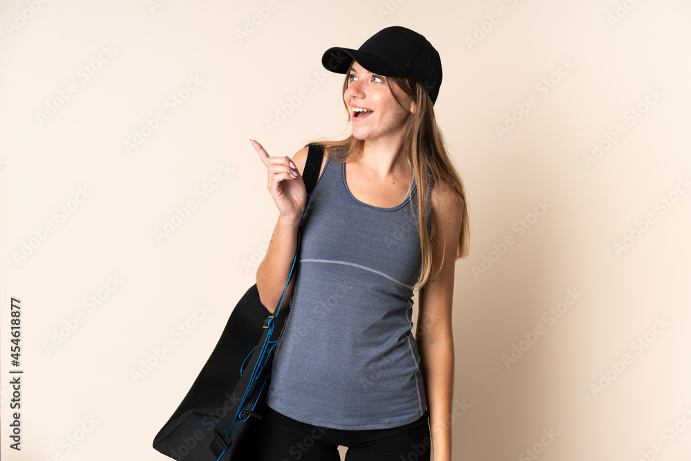 Young sport Lithuanian woman holding a sport bag isolated on beige background intending to realizes the solution while lifting a finger up Young sport Lithuanian woman holding a sport bag isolated on beige background intending to realizes the solution while lifting a finger up