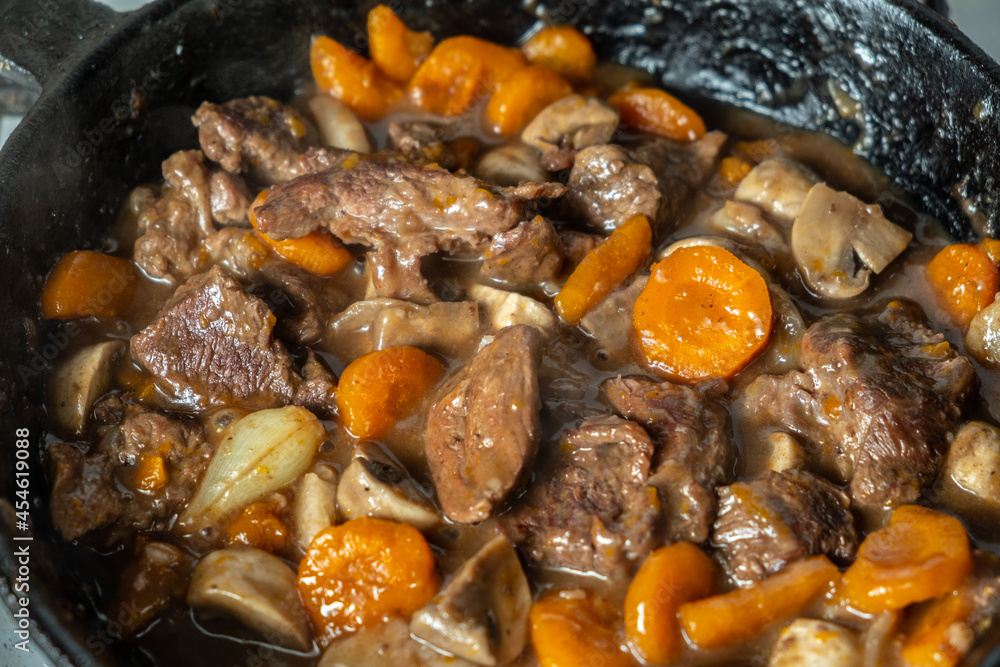 Ready of Beef Burgeoning beef dish in a frying pan. meat, carrots and onions and mushrooms. Appetizing sauce. Slow food concept. Close-up Ready of Beef Burgeoning beef dish in a frying pan. meat, carrots and onions and mushrooms. Appetizing sauce. Slow food concept. Close-up