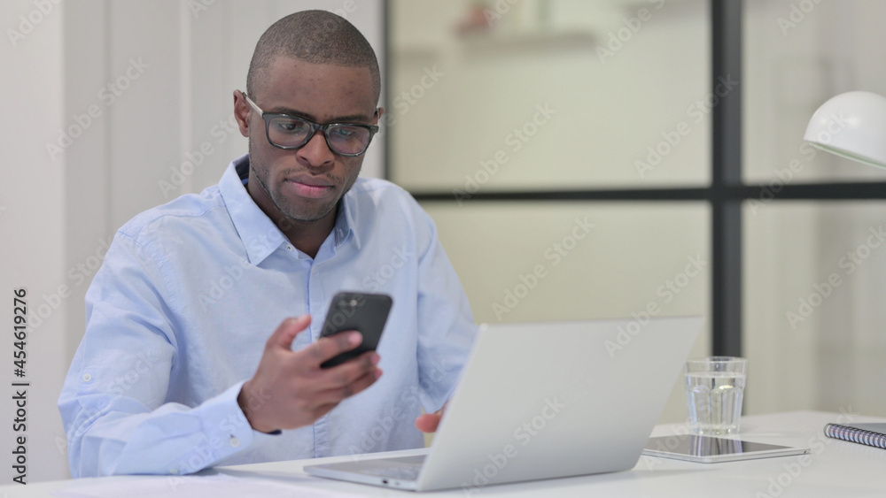 African Man Using Smartphone and Laptop for Work African Man Using Smartphone and Laptop for Work