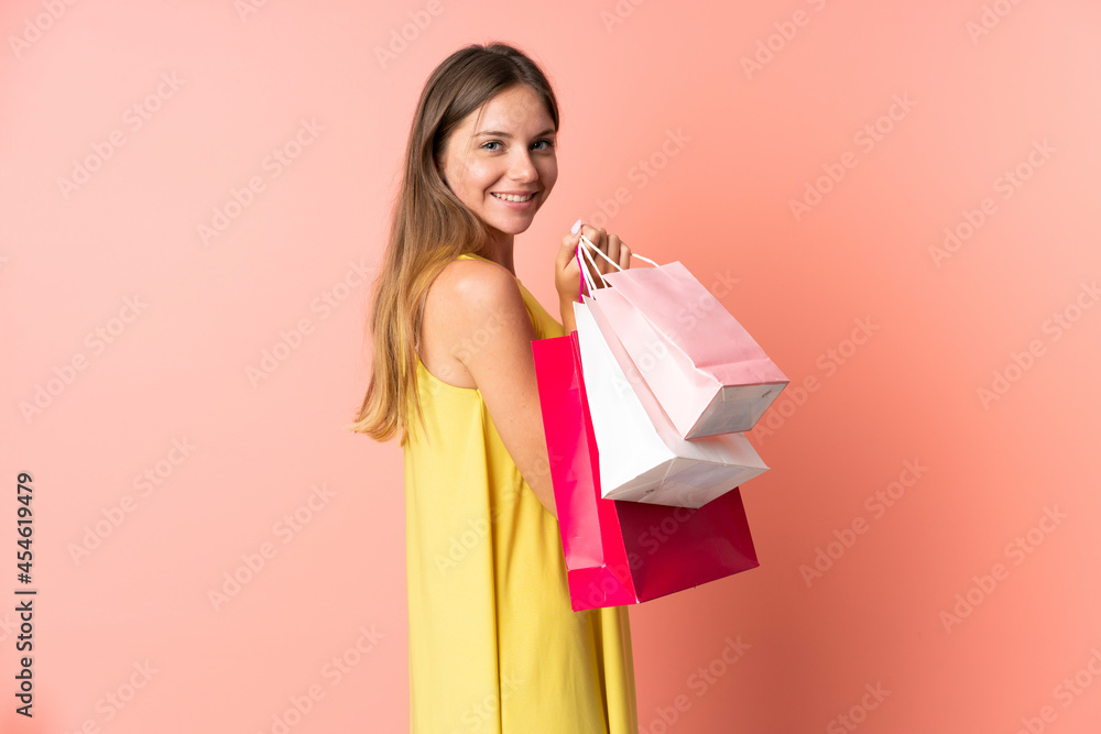 Young Lithuanian woman isolated on pink background holding shopping bags and smiling