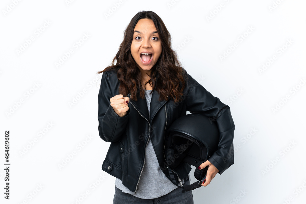 Young woman holding a motorcycle helmet over isolated white background celebrating a victory in winner position Young woman holding a motorcycle helmet over isolated white background celebrating a victory in winner position
