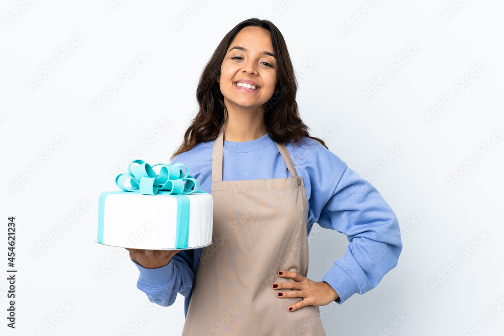 Pastry chef holding a big cake over isolated white background posing with arms at hip and smiling Pastry chef holding a big cake over isolated white background posing with arms at hip and smiling