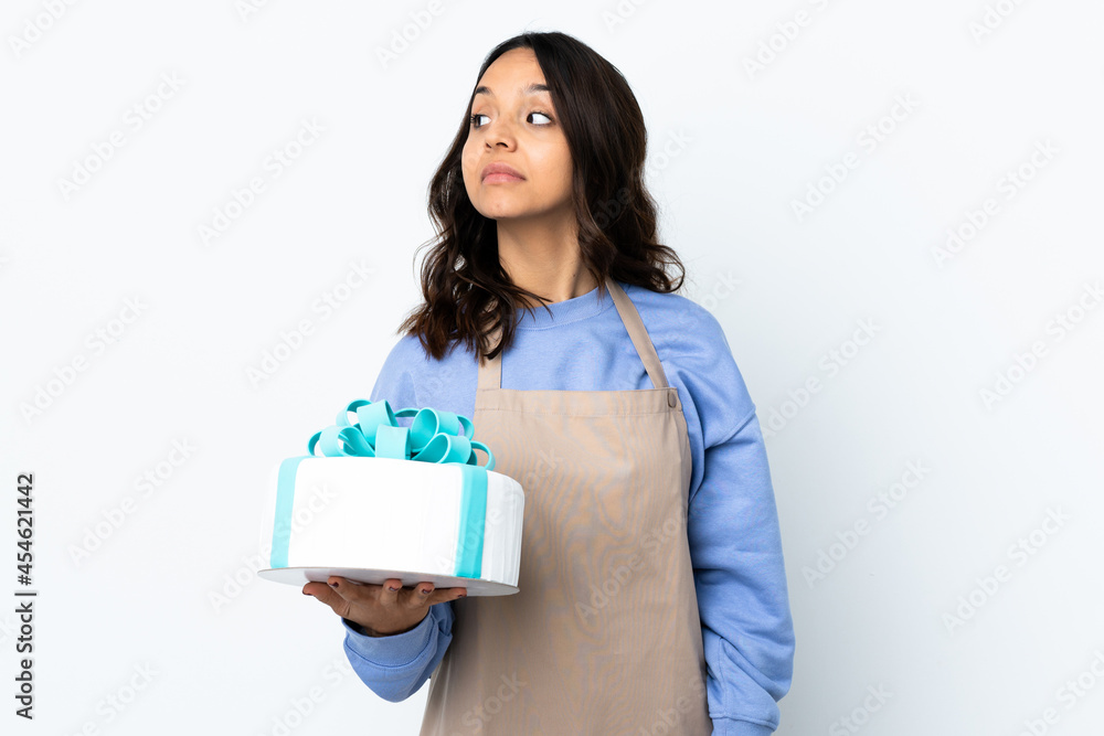 Pastry chef holding a big cake over isolated white background making doubts gesture looking side Pastry chef holding a big cake over isolated white background making doubts gesture looking side