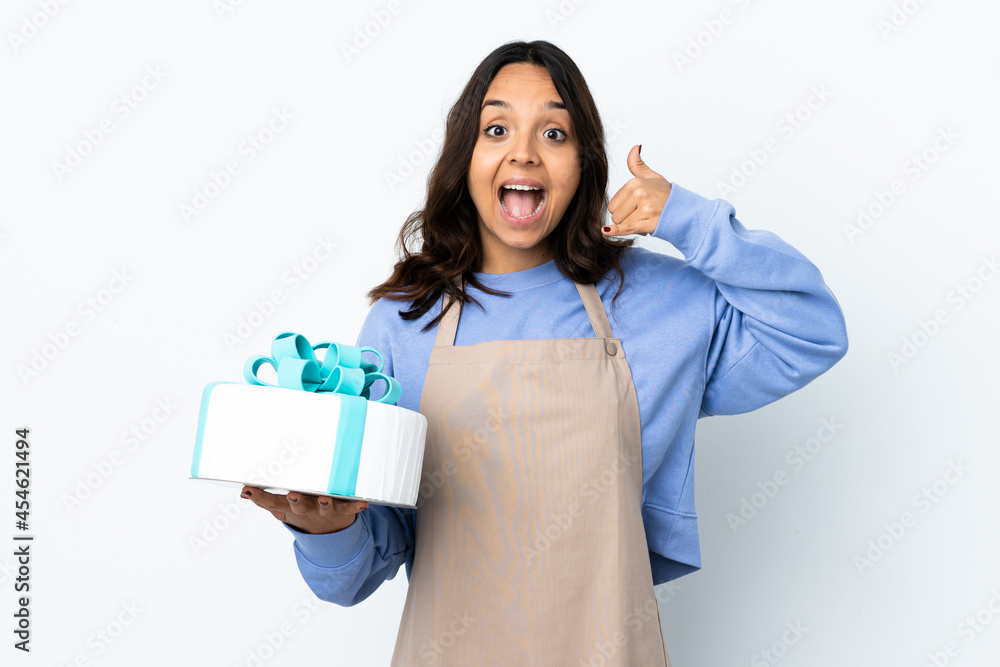 Pastry chef holding a big cake over isolated white background making phone gesture. Call me back sign Pastry chef holding a big cake over isolated white background making phone gesture. Call me back sign