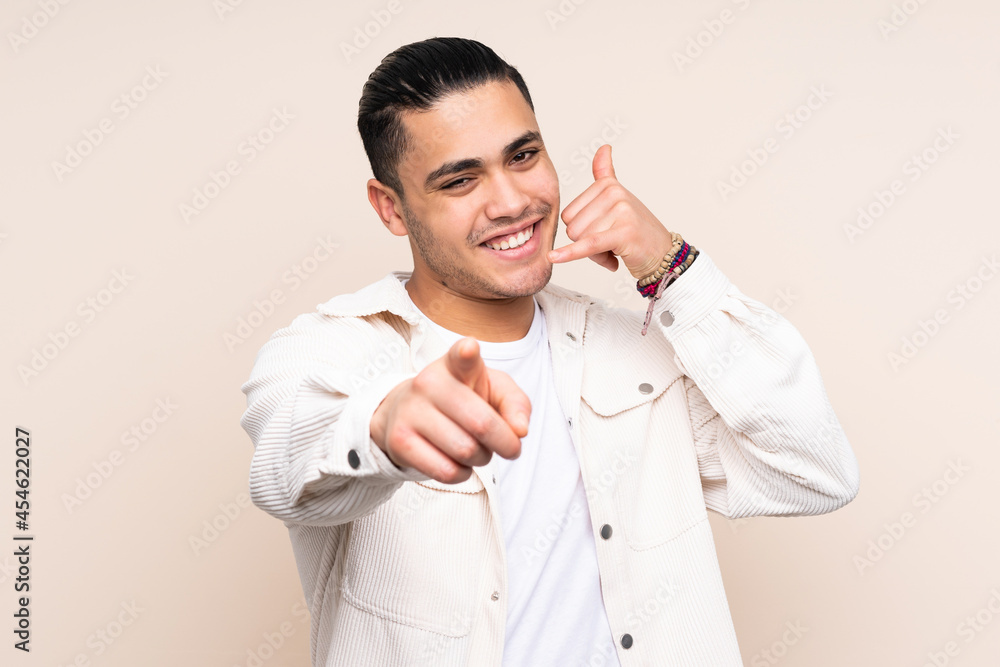 Asian handsome man over isolated background making phone gesture and pointing front Asian handsome man over isolated background making phone gesture and pointing front