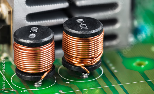 Closeup of electronic coils and metal cooler on green printed circuit board detail. Ferromagnetic inductors with copper wire winding or aluminum heat sink on PCB. Components in electrical engineering. photo