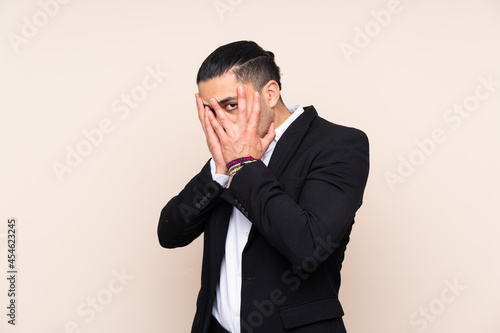 Asian business man isolated on beige background covering eyes and looking through fingers