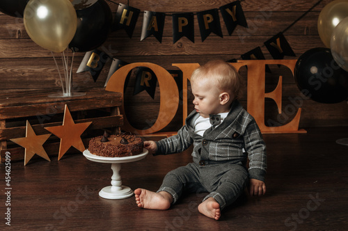 a baby boy in a gray suit eats a chocolate cake on a festive background