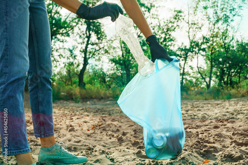 Woman puts a plastic bottle in a trash bag. Garbage collection in the nature.