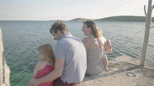 Slow motion - Young family with small children enjoying their vacations while sitting on the dock by the sea