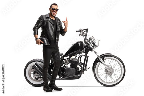 Cool biker with a chopper holding helmet and gesturing rock and roll sign