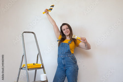 woman chooses between roller and brush on background ladder and gray cement wall. choice of tools for painting and priming. beginner in renovation photo