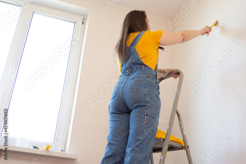 Young Professional repair woman with priming or painting the wall with brush. Independent single female makes repairs apartment  photo