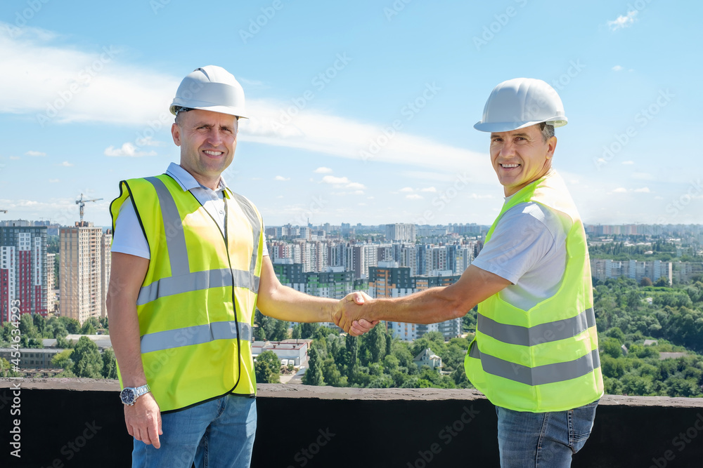 Architect and construction engineer shaking hands on the roof of a building at a construction site outdoors. Construction cooperation concept